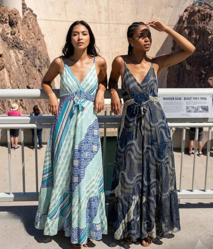 wo women wearing the Sari Maxi Dress in aqua patchwork geometric print and navy dotted swirl print, leaning against a railing at Hoover Dam.