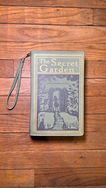 Book-shaped clutch with 'The Secret Garden' design on a wooden surface