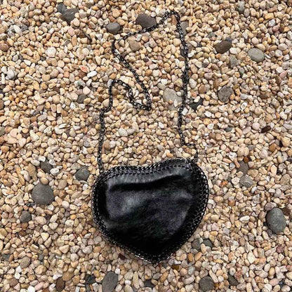 Black heart shape purse with crossbody chain laying in a bed of stones