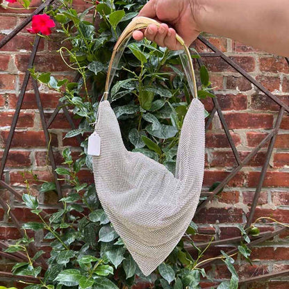 Silver rhinestone bag with faux gold handle against green foliage and brick wall
