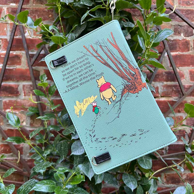 Teal notebook with Winnie the Pooh illustration on a plant with a brick wall background