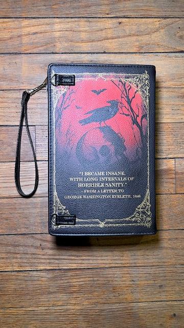Book-shaped clutch with a raven design showcasing the back cover with Edgar Allen Poe quote on a wooden surface