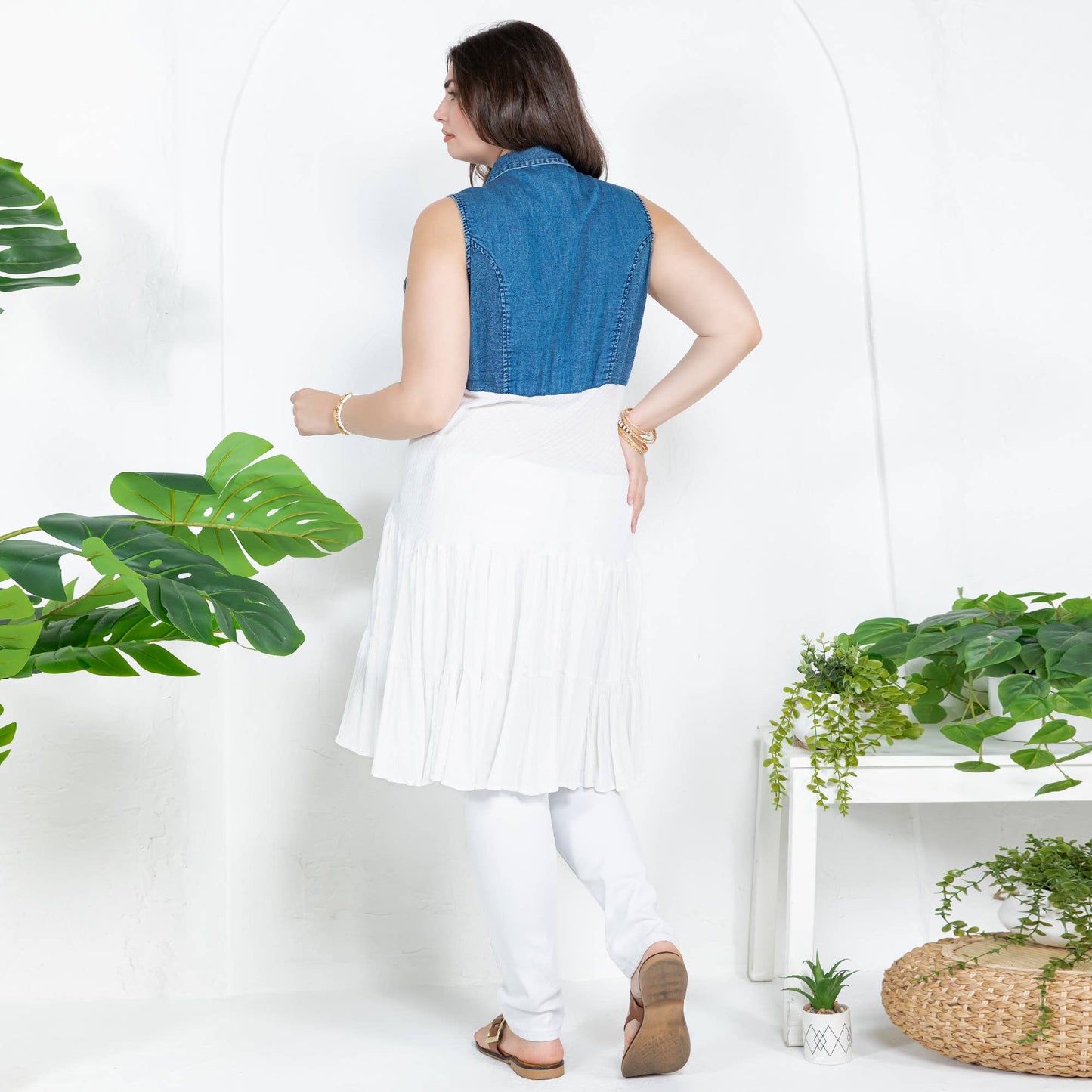 Woman wearing a blue denim top and white skirt with plants in the background