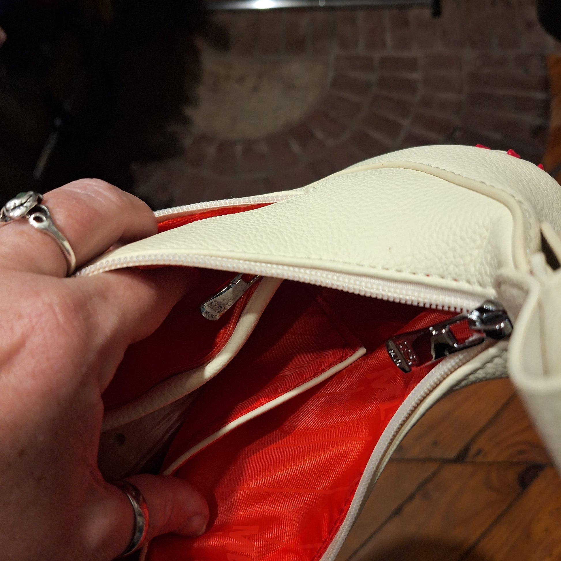 Hand opening a white zipper on the white hobo bag a red garment with a blurred background