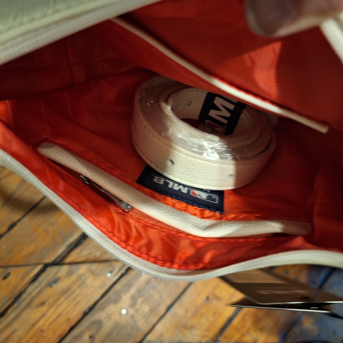 Close-up of the white phillies hobo bag with red lining and a belt inside, on a wooden floor.