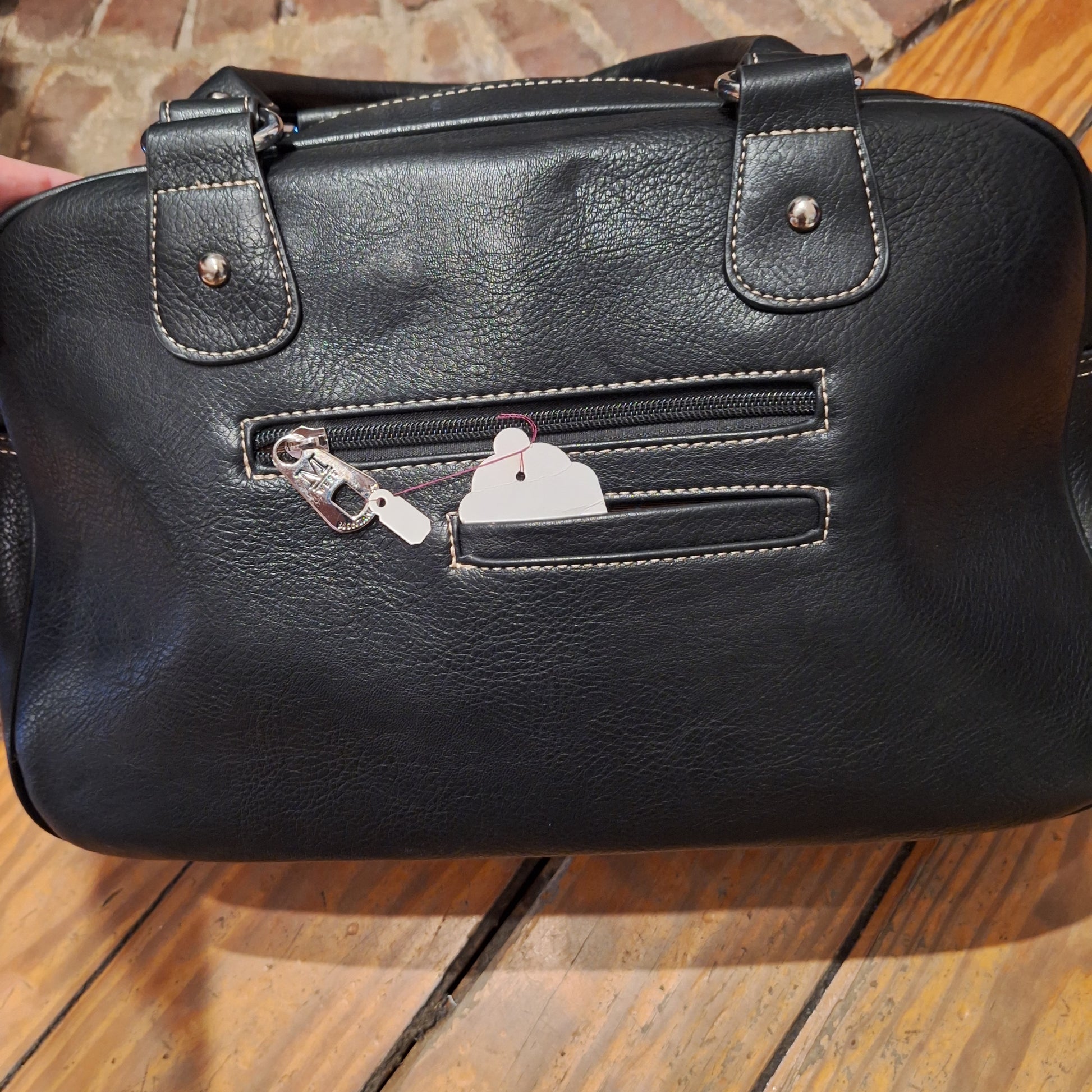 Black leather handbag with a small white dog-shaped charm on a wooden surface.