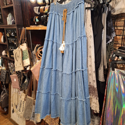 Flowy light blue tiered denim maxi skirt with tassel waist tie, hanging on hanger