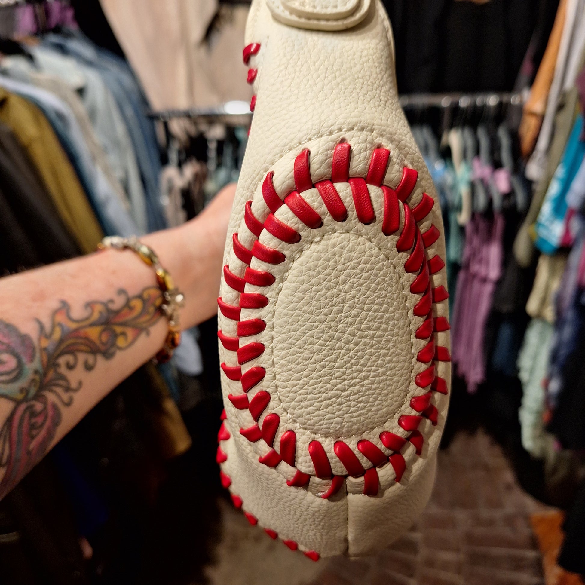 Baseball-shaped pillow with red stitching held in front of a clothing rack.